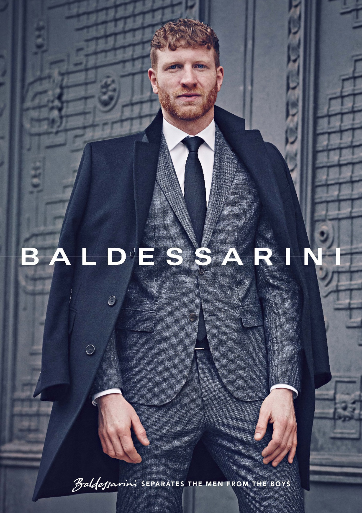 Baldessarini campaign: man in a grey suit and dark coat before an ornate steel door