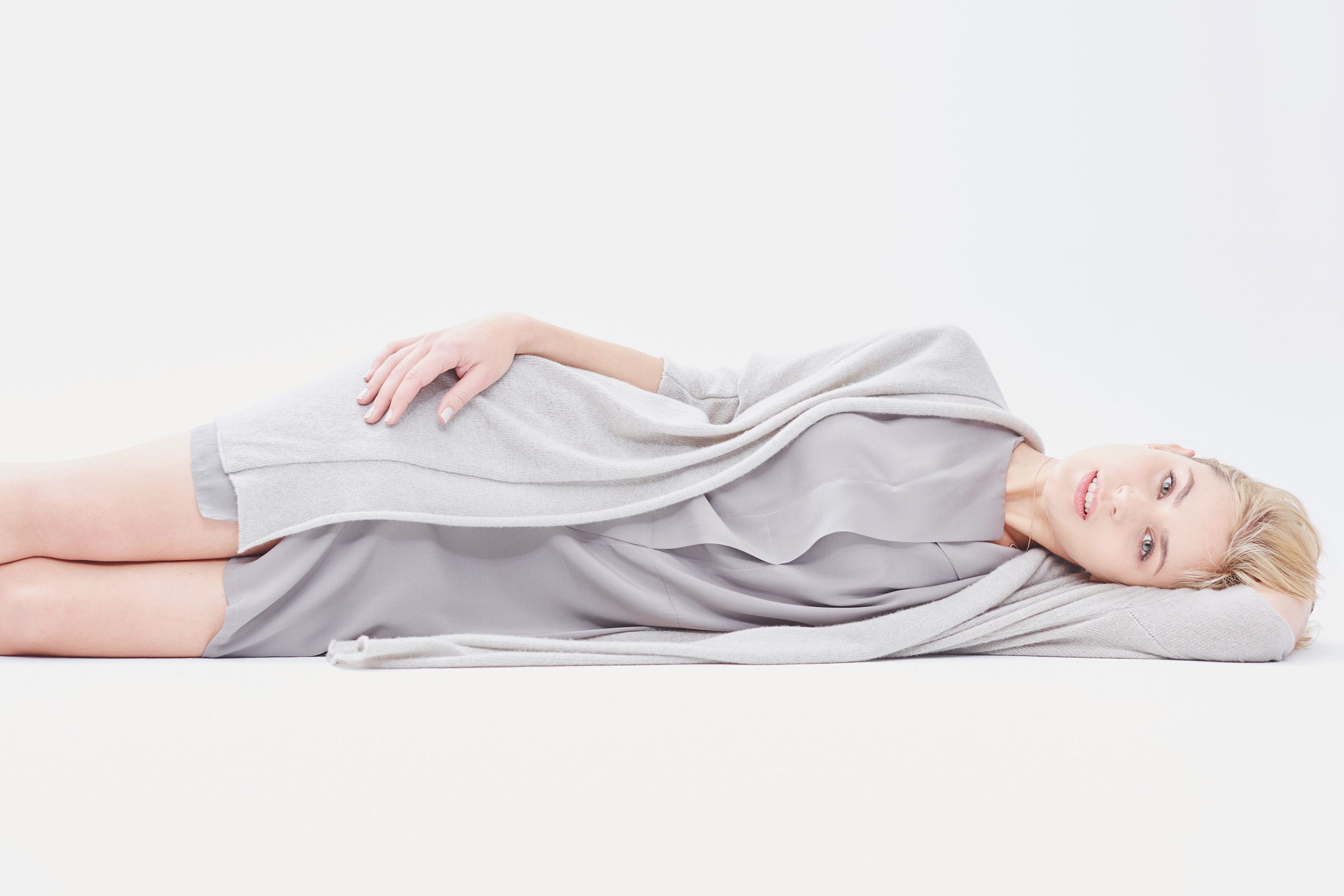 Model lying on her side in grey knitwear against a white background